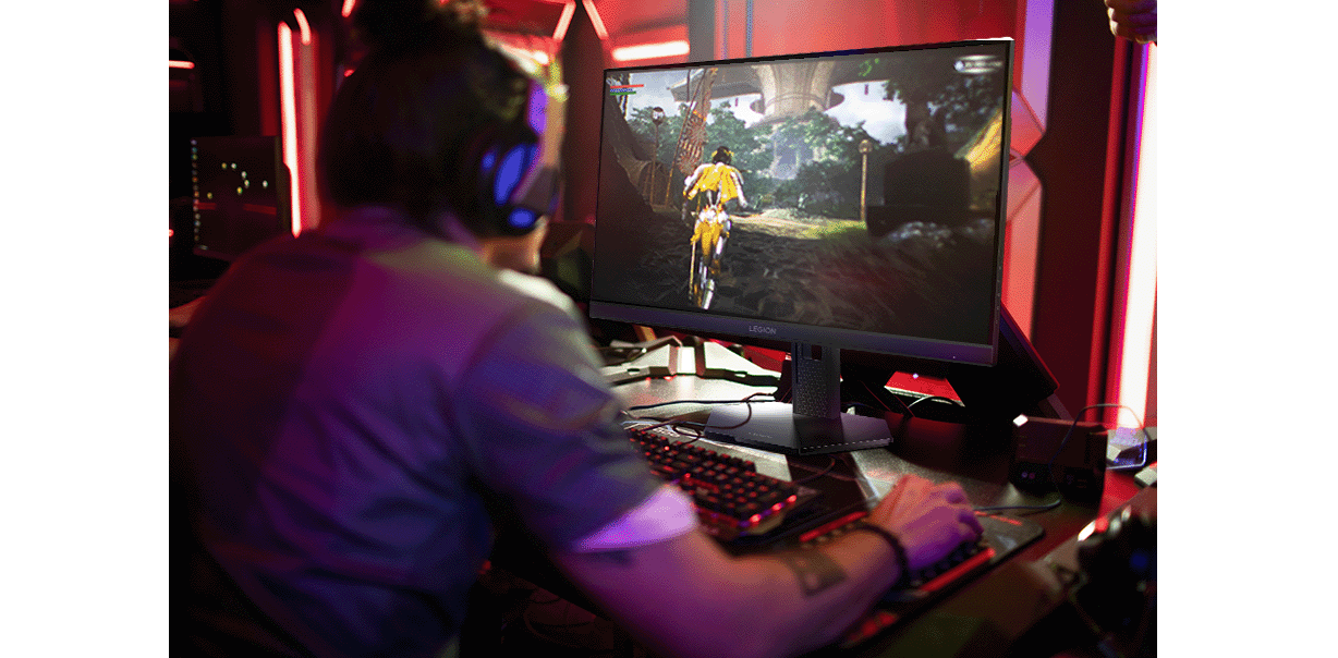 A person wearing headphones is gaming on a Lenovo Legion-27q-11 monitor in a room with red and purple lighting. מסך מחשב גיימינג Legion 27Q-11 מבית Lenovo