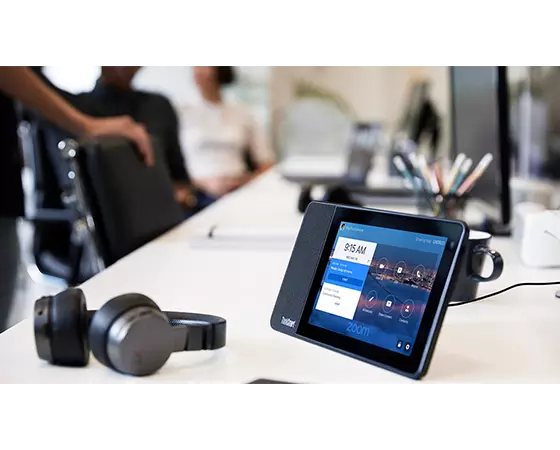 ThinkSmart View Zoom sitting on white desk showing time and calendar on screenfill with X1 headphones laying beside it.