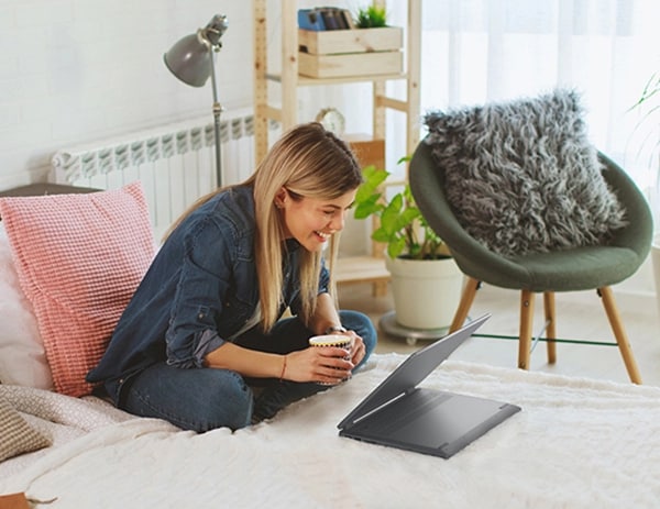 Woman sitting cross-legged on bed using IdeaPad Flex 5i in stand mode.