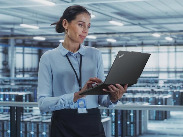 Person standing in data center, holding ThinkPad E14 Gen 5 (14â€³ Intel) laptop in one hand and looking at the display