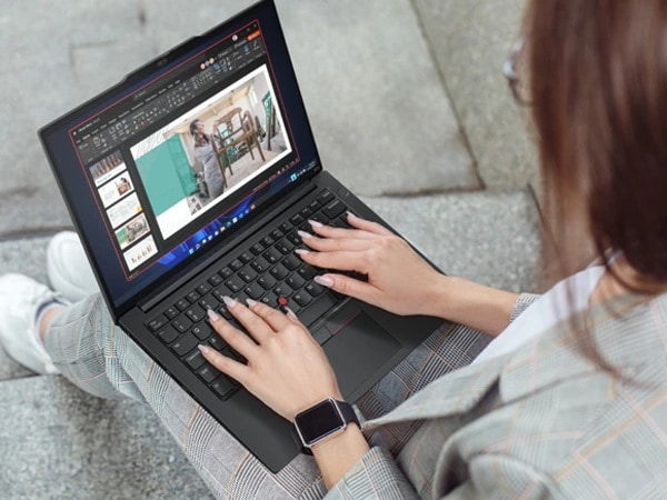 Over-the-shoulder, close-up view of person sitting on concrete stairs, holding ThinkPad E14 Gen 5 (14â€³ Intel) laptop in their lap, with both hands on keyboard, looking at slideshow on the display