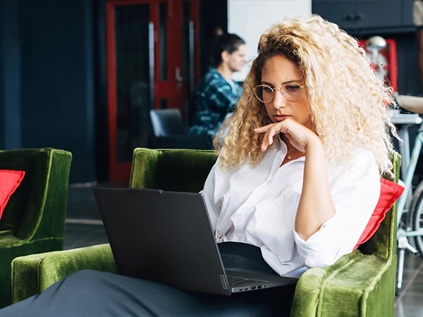 Front view of a person sitting on a couch in public area & working on the Lenovo ThinkPad T14 Gen 5 (14 inch Intel) Eclipse Black laptop.